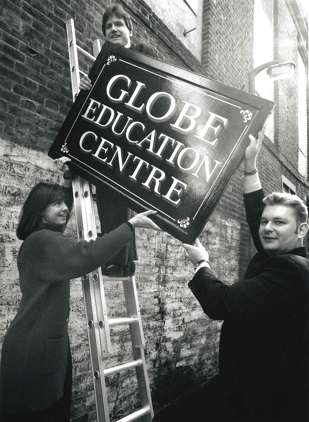Three people lift a sign saying Globe Education Centre up a ladder.