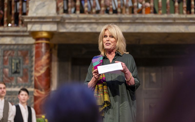 A woman stands on a stage reading from a piece of paper