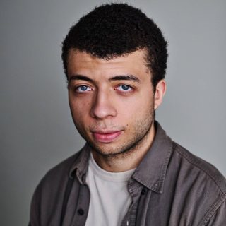 Joshua Griffin wearing a grey shirt over a white t-shirt and looking directly at the camera.