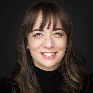 Patricia Rodriguez wearing a black turtle neck and smiling directly at the camera in front of dark background.