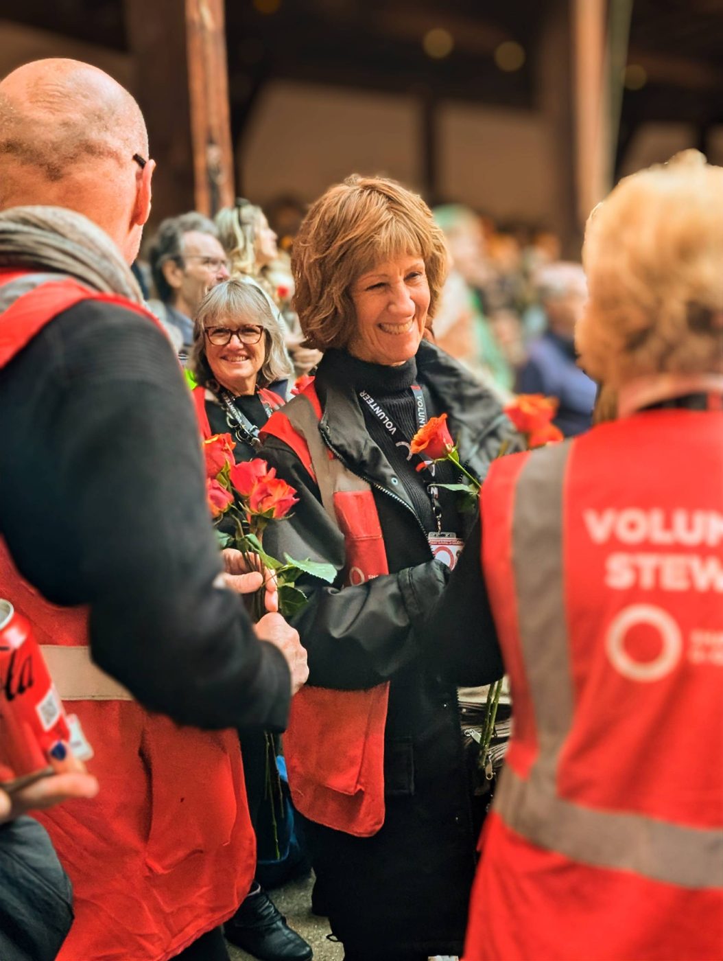 Volunteer stewards stand inside the Globe Theatre holding roses.