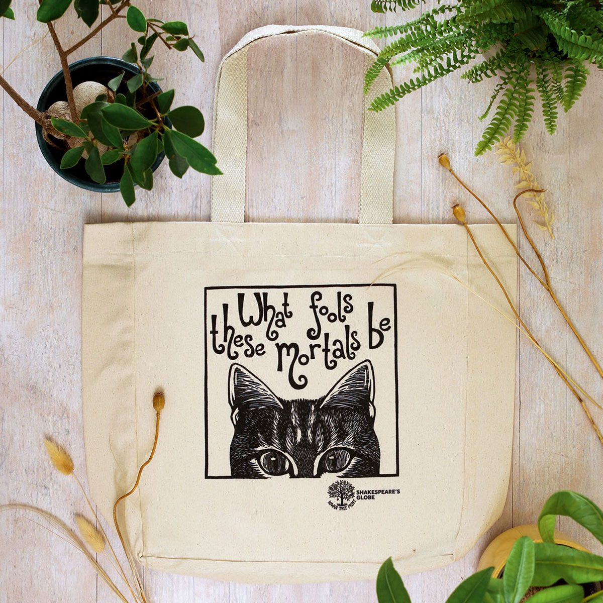 A cream tote bag with a black print of a cat and the quote 'What fools these mortals be'.