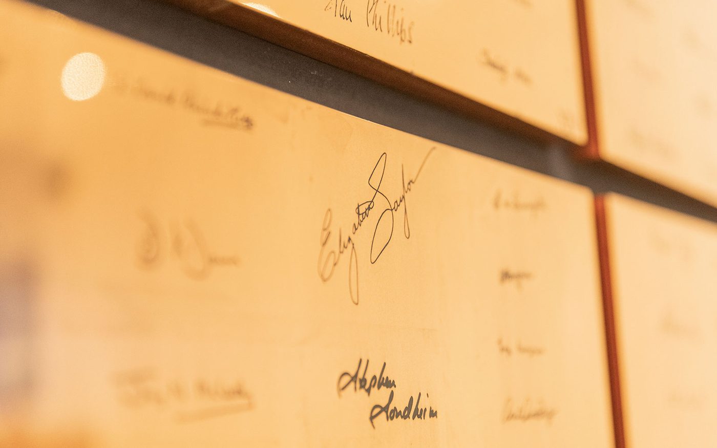 A bronze square with engraved signatures on it. The camera is focused on the signatures of Elizabeth Taylor and Stephen Sondheim.