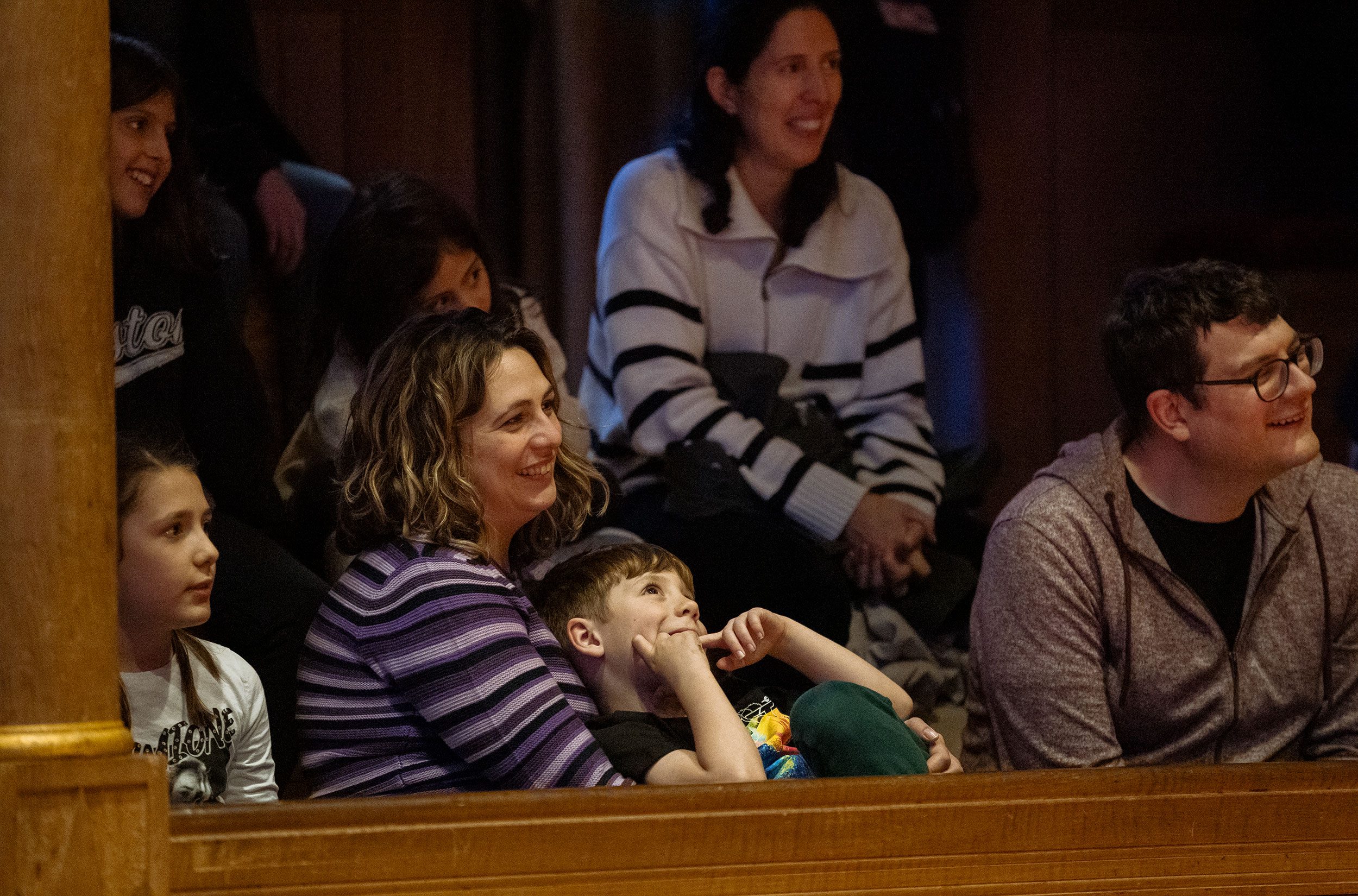 Parents and children inside a wooden theatre watching a performance.