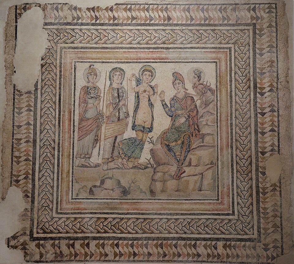 An ancient Roman mosaic, showing a line of three women and a man dressed in Roman tunics. The mosaic has an ornate geometric border around it, and some patches of the mosaic are missing.
